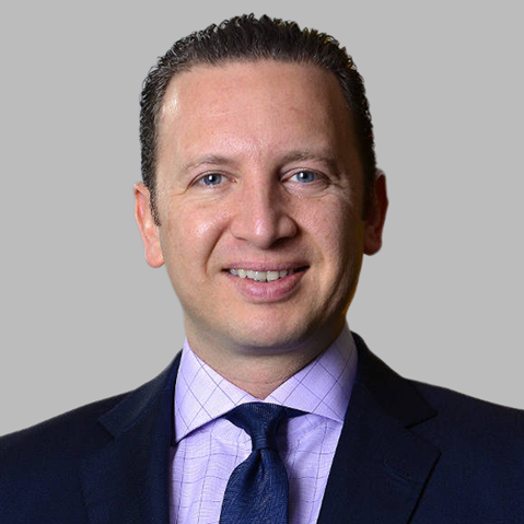 A professional man in a suit with a collared shirt and tie, set against a plain grey background.