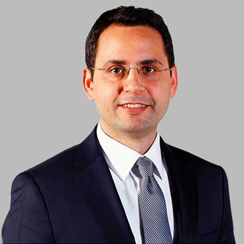 A businessman in a dark suit and tie poses against a plain background, exuding professionalism.