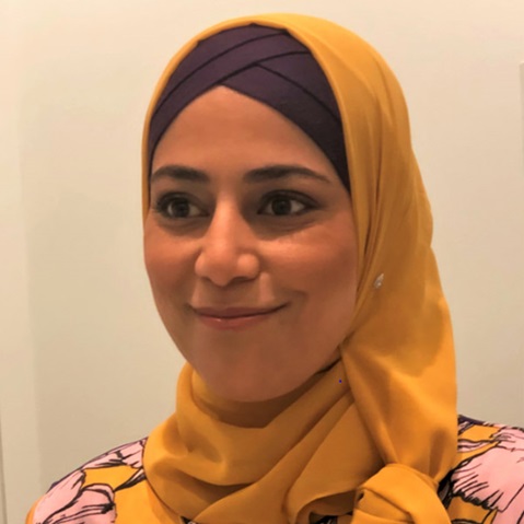A person wearing a bright yellow hijab and a patterned top stands against a light background.